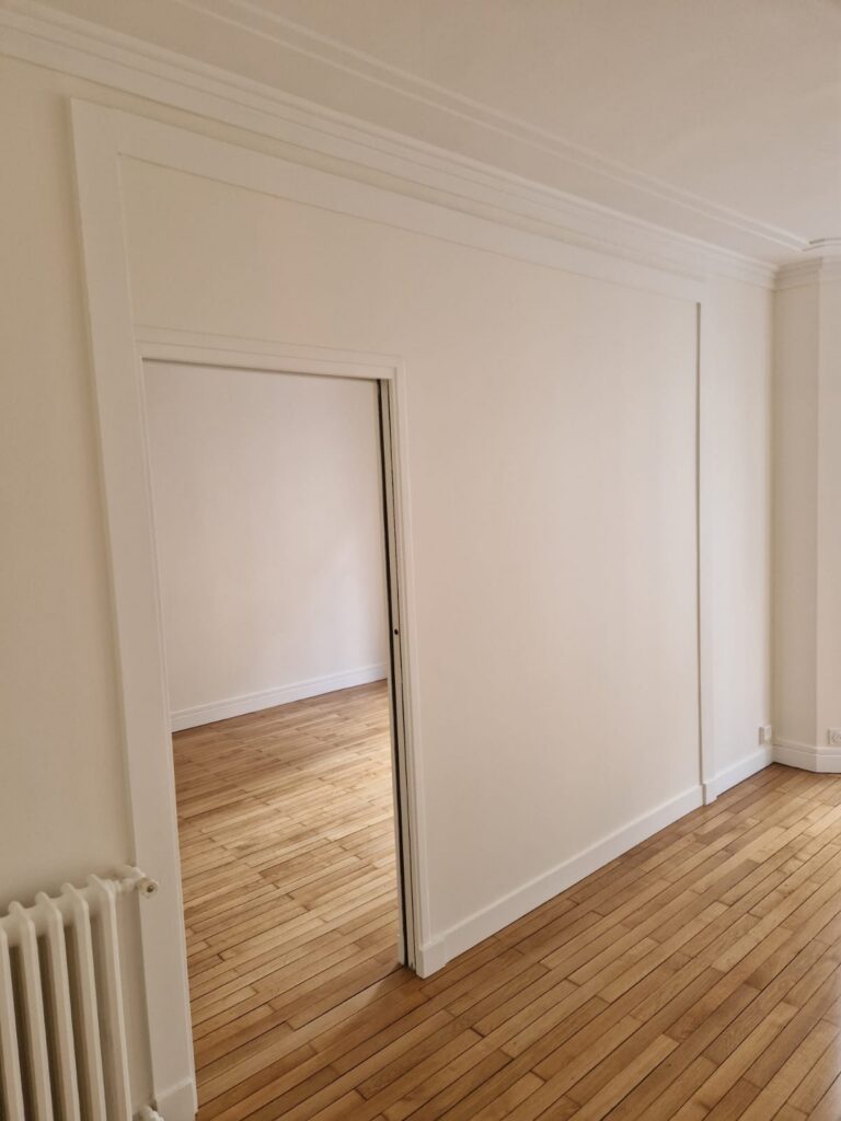 Couloir ou entrée rénovée Murs blancs, parquet bois, porte intérieure blanche, finitions soignées.