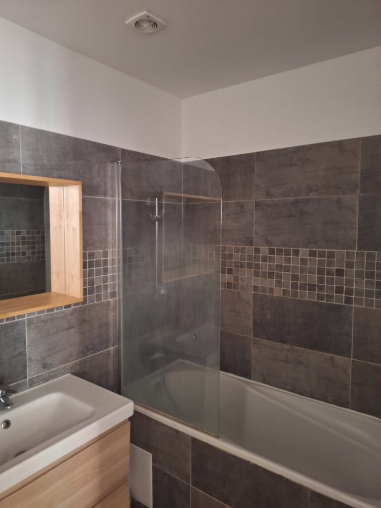 Salle de bain rénovée Baignoire, carrelage mural foncé, faïence moderne, travail de rénovation.