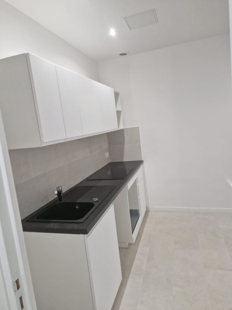 Cuisine rénovée et moderne Meubles blancs, plan de travail foncé, évier, sol clair, aménagement intérieur.