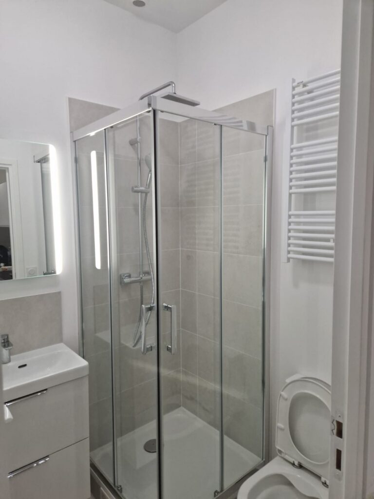 Salle de bain avec douche vitrée Douche à l’italienne, paroi en verre, carrelage clair, rénovation intérieure.
